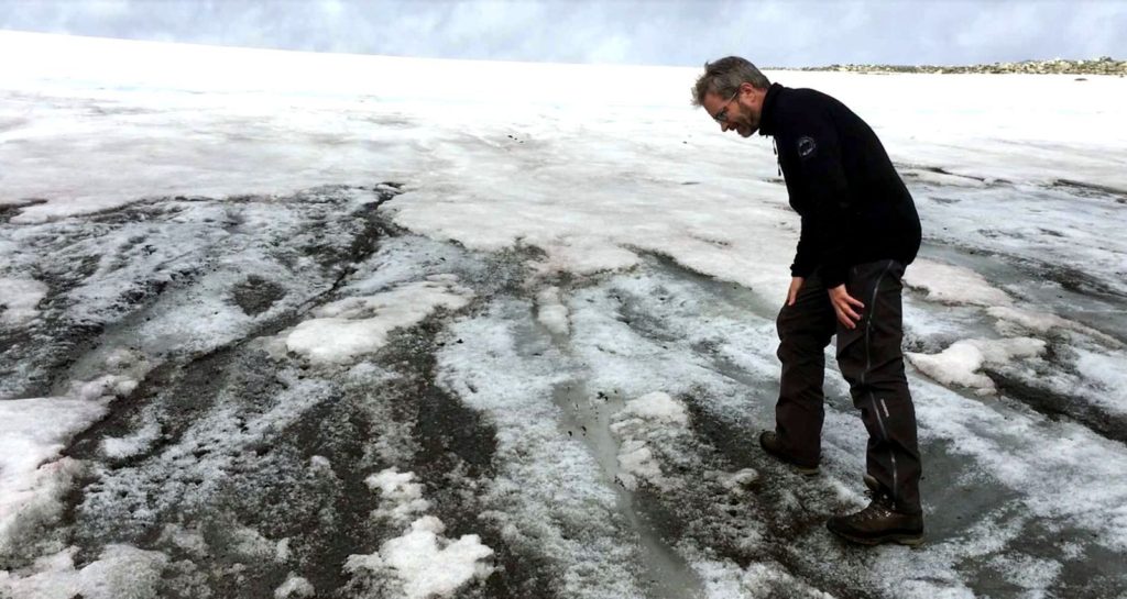 Lars Pilø standing on ancient dark ice, exposed on the surface of on ice patch 